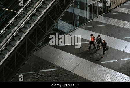 Male entrepreneur with female colleagues discussing while walking by escalator Stock Photo