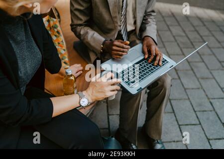 Cropped image of male and female colleagues discussing over laptop while sitting on bench Stock Photo