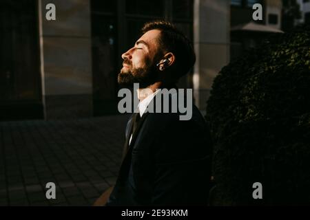 Male entrepreneur listening music through wireless earphones on footpath Stock Photo