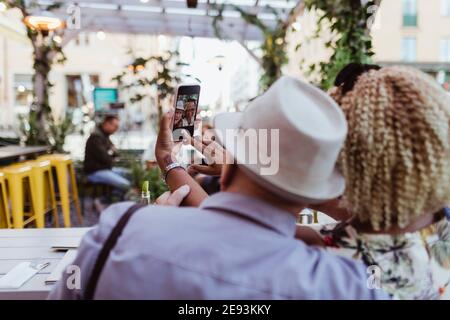 Rear view of senior couple taking selfie in sidewalk cafe Stock Photo