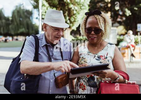 Smiling senior couple using digital tablet on street during sunny day Stock Photo