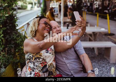 Cheerful heterosexual couple taking selfie on smart phone at cafe Stock Photo