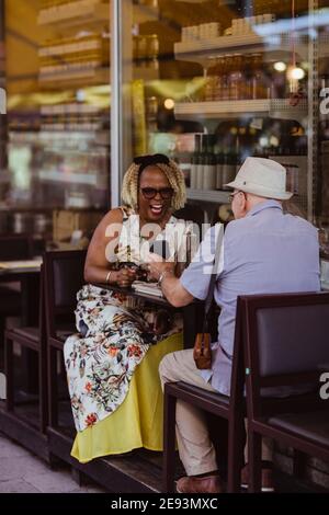 Senior woman laughing while man showing smart phone at sidewalk cafe Stock Photo