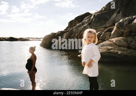 Girl at sea, pregnant mother in background Stock Photo