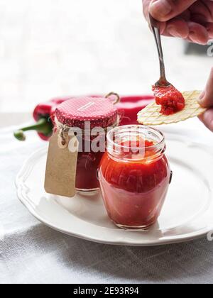 Ajvar, traditional Balkan roasted red pepper relish in glass with female hand holding spoon on white plate and background. Shallow depth of field. Stock Photo