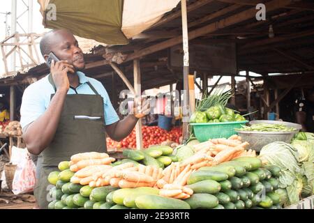 an african market man selling fruits and vegetables making a phone call Stock Photo