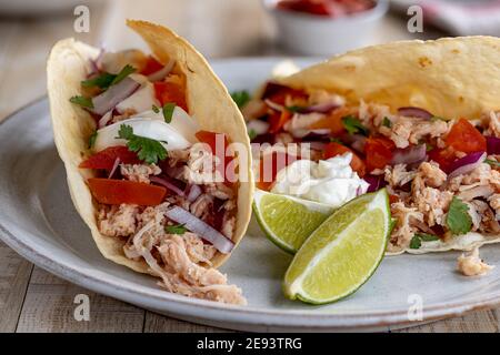 Tacos with pulled chicken, tomato, onion and sour cream and lime wedges on the side on a plate Stock Photo