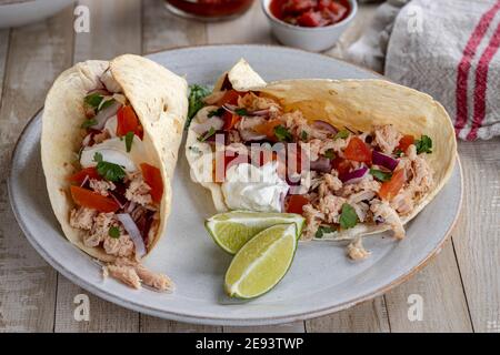 Tacos with pulled chicken, tomato, onion and sour cream and lime wedges on the side on a plate Stock Photo