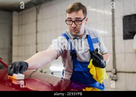 Car detailing - Man applies nano protective coating or wax on red car. Covering car bonnet with a liquid glass polish. Stock Photo