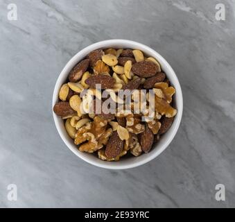 Assorted nuts in a white bowl on a fake marble tile top view. Stock Photo