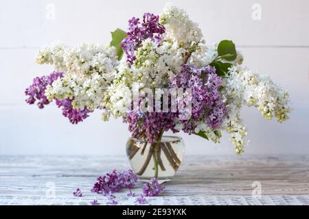 White lilac and purple lilac in glass vase on wooden table. Spring branches of blooming lilac festive bouquet of flowers. Stock Photo