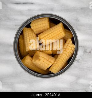 Overhead view of an open can filled with organic baby corn on a gray marble background.