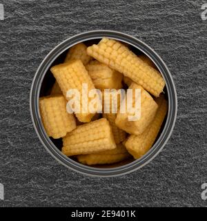 Overhead view of an open can filled with organic baby corn on a gray slate background.