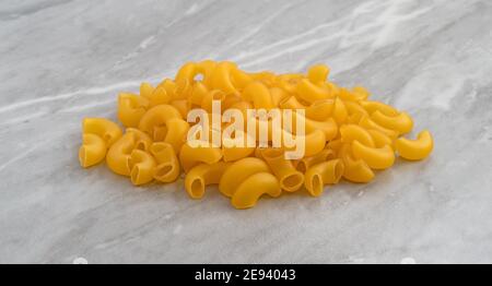 Side view of a portion of organic elbow macaroni atop a gray marble countertop illuminated with natural light. Stock Photo