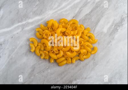 Pile of organic elbow macaroni atop a gray marble countertop illuminated with natural light. Stock Photo