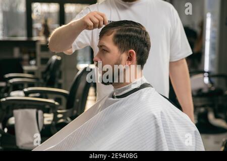 Close up of client of master barber, stylist during getting care and new look of hairstyle. Professional occupation, male beauty and self-care concept. Soft colors and focus, vintage. Stock Photo