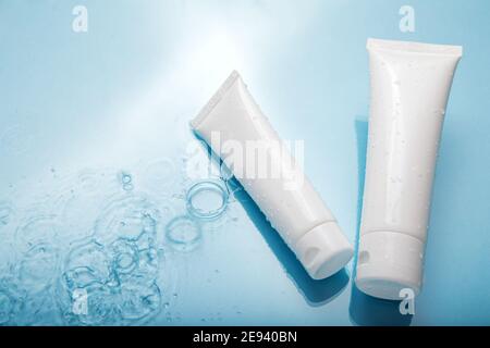 White cosmetic products in tubes on color blue background with water drops. Mock up skincare cosmetic packages on water surface. Natural moisturizing Stock Photo