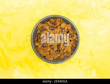Top view of a bowl filled with bran flakes and raisins breakfast cereal on a yellow painted background. Stock Photo