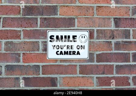 Sign with a smiley face saying you are being recorded on a brick wall. Stock Photo