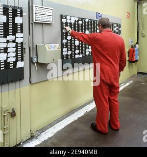 Historical 1992 archive back view of factory worker wearing overalls using clocking in or out card system to validate time working on wall mounted machine for wages calculations archival1900s image how we were in 90s Essex England UK Stock Photo