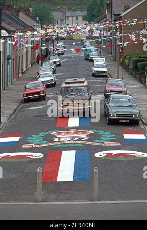 Looking down on parked 1970s cars below overhead bunting and 1977 artistic crown decoration painted onto tarmac surface on no through road at end of a residential street to celebrate Queen Elizabeth ii Silver Jubilee with welsh dragon emblem & red white and blue decorations in City and County of Swansea South Wales UK Stock Photo