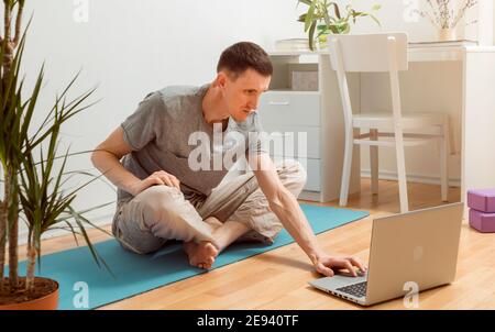 Young man doing yoga exercise online using laptop at home. Stock Photo