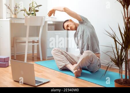 Young man doing yoga exercise online using laptop at home. Stock Photo