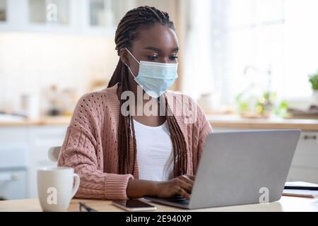 Young black business woman working from home with laptop, wearing medical mask Stock Photo