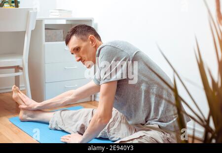 Young man doing yoga exercise online using laptop at home. Stock Photo