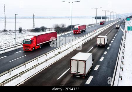 Highway transportation with a convoy of Lorry trucks passing trucks in a snowy winter landscape Stock Photo