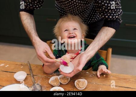 A young toddler having fun helping his dad bake cakes in the kitchen. Stock Photo