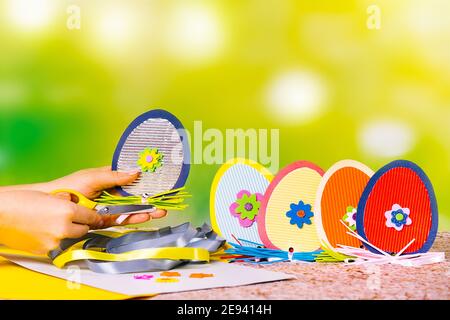 Decorative handcraft eggs made of handmade colored cardboard. Material and hands with an illuminating scissors on a green background. Preparing for a Stock Photo