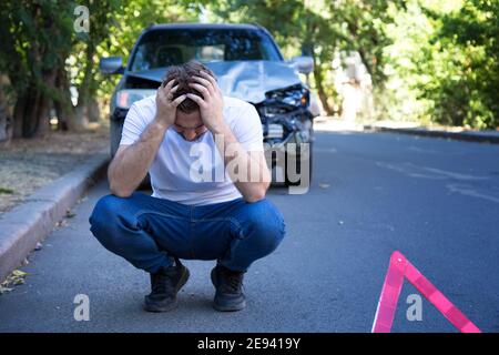 Driver man in front of wrecked car in car accident. Scared man holding his head after auto crash. Tragedy car collision. Dangerous road traffic Stock Photo