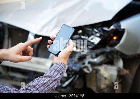 Man holds mockup mobile phone screen in hands after car accident. Calling insurance service in web app to place of car accident. Smartphone in front Stock Photo