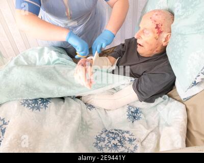 The ninety five year old has the injured arm bandaged at his house by a visiting district nurse.He is unable to leave his bed or house due to frailty Stock Photo