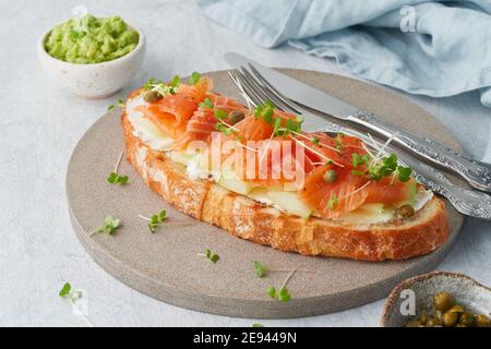 Two open sandwich, toast with salmon, cream cheese, avocado, cucumber slices on white concrete table. Stock Photo