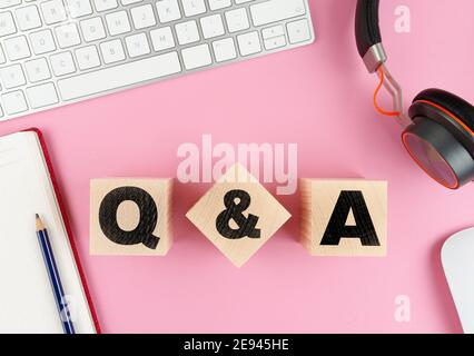 Q and A on wooden blocks on pink desk with computer keyboard, headphones and notepad Stock Photo