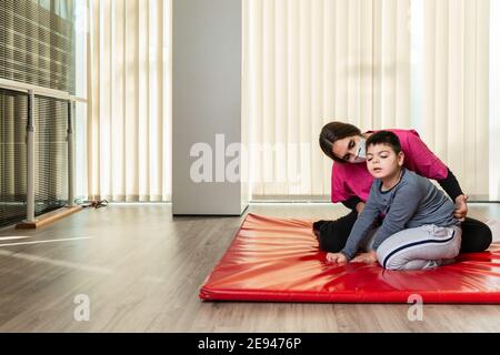 disabled child and physiotherapist on a red gymnastic mat doing exercises. pandemic mask protection Stock Photo