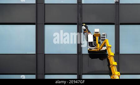 Male window cleaner cleaning glass windows on modern building high in the air on a lift platform. Worker polishing glass high in the air Stock Photo
