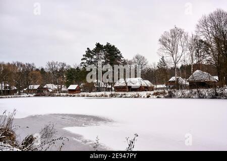 Radom, Poland -  January 15, 2021. Old wooden farm buildings seen across frozen pond in Radom Village Museum. Stock Photo