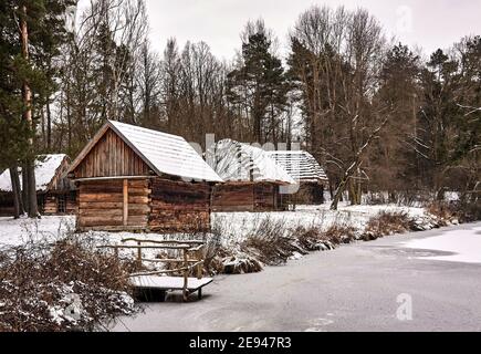 Radom, Poland -  January 15, 2021. Old wooden farm buildings seen across frozen pond in Radom Village Museum. Stock Photo