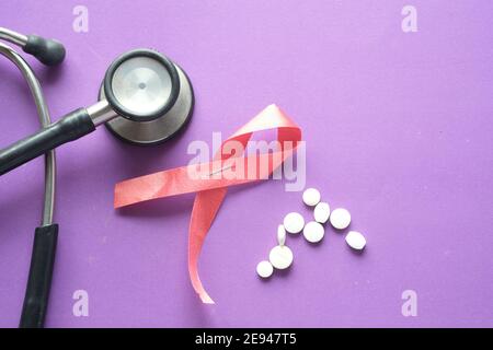 Red ribbon HIV, and stethoscope on purple background. Stock Photo