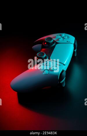 Modern white gamepad illuminated in red and blue. Game controller for video games and e-sports on a dark background. Stock Photo