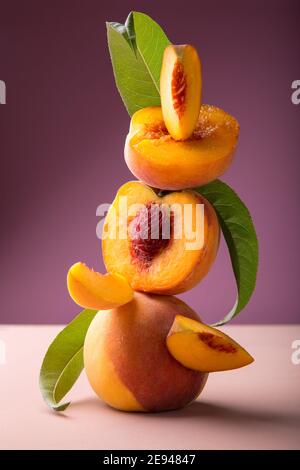 Flying fresh ripe peach in slices and whole fruits with green leaves. Peach fruit levitation on pink color background. Minimalistic composition with Stock Photo