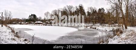 Radom, Poland -  January 15, 2021. Old wooden farm buildings seen across frozen pond in Radom Village Museum. Stock Photo