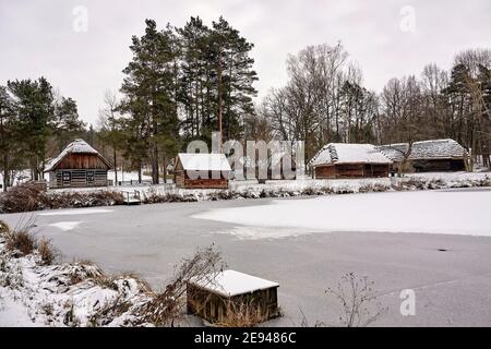 Radom, Poland -  January 15, 2021. Old wooden farm buildings seen across frozen pond in Radom Village Museum. Stock Photo