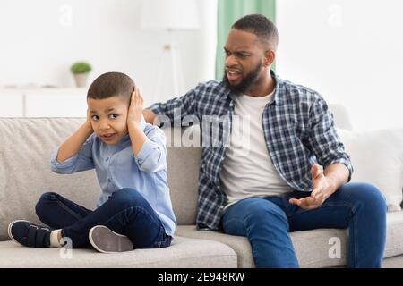 Irritated Black Father Shouting At Unhappy Little Son At Home. Stock Photo