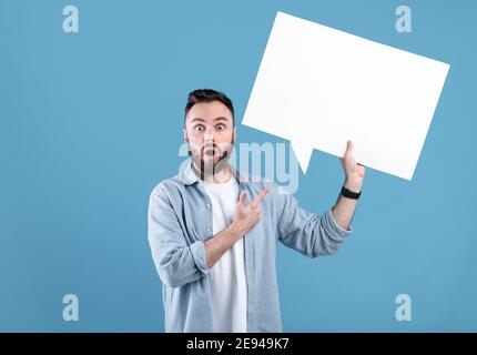 Shocked young guy pointing at empty speech bubble with space for your design over blue studio background, mockup Stock Photo