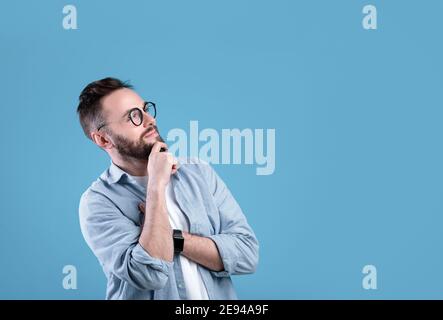 Pensive Caucasian guy thinking over decision or problem, looking at empty space over blue studio background Stock Photo