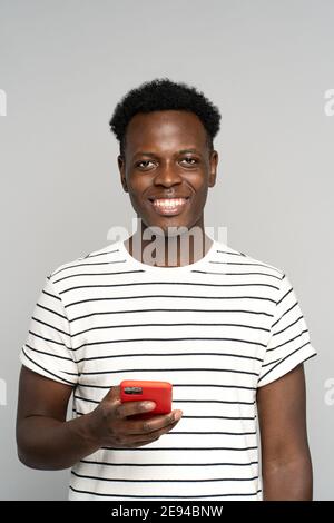 Happy African millennial man in glasses, holding mobile phone, isolated on studio grey background Stock Photo